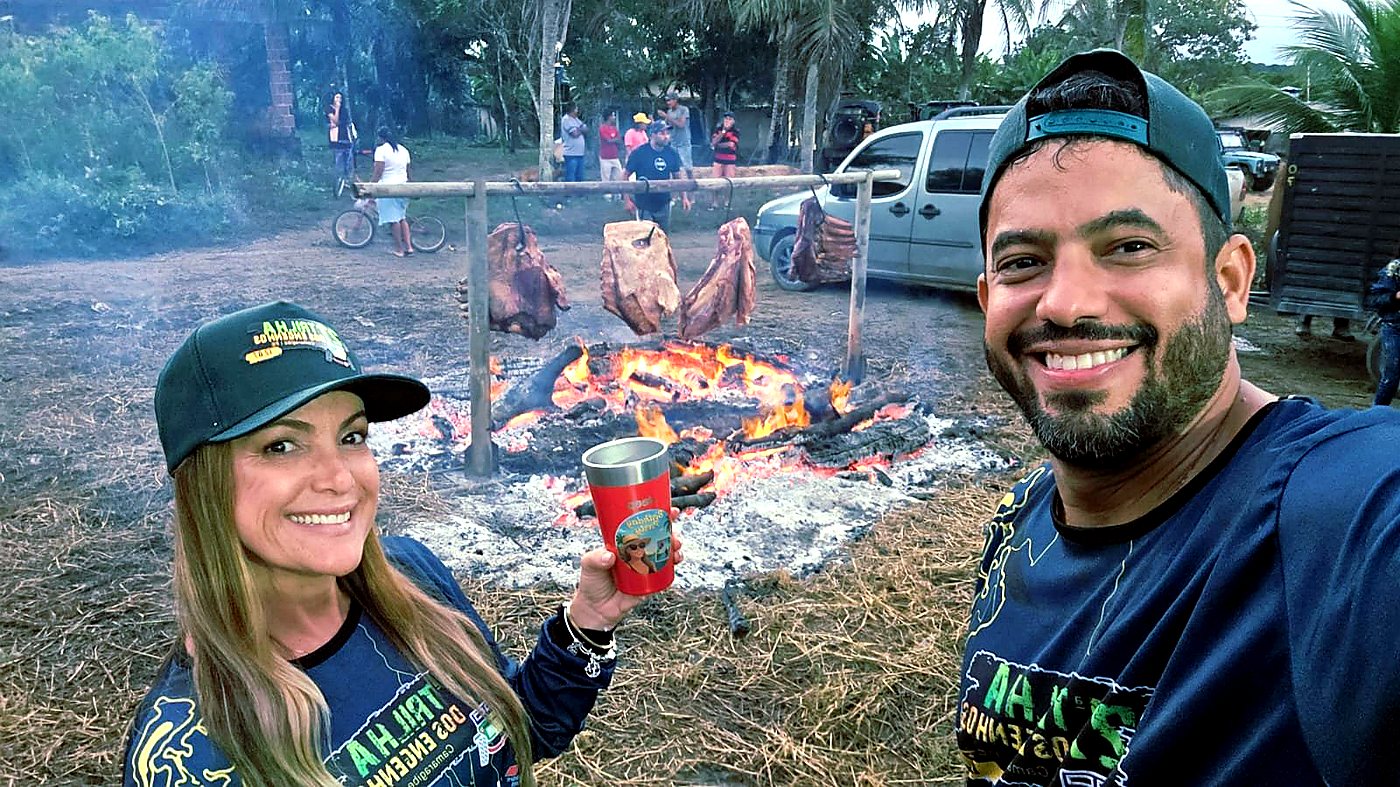 Casal sorrindo com camisas oficiais em frente ao fogo de chão