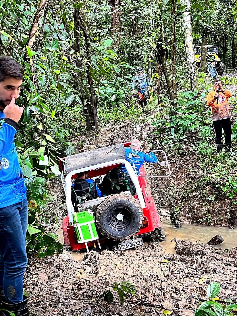 Jeep vermelho descendo barranco íngreme guiado pela equipe Anarquia Jipeira, com organizador narrando ao microfone