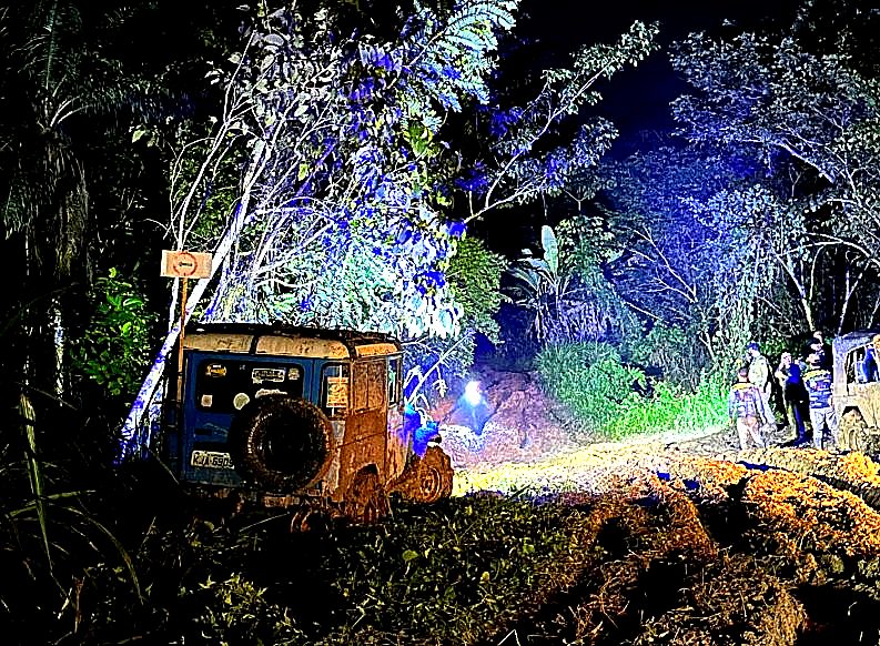 Trilha noturna cinematográfica — jeep azul iluminado pela luz da floresta, equipe trabalhando ao fundo