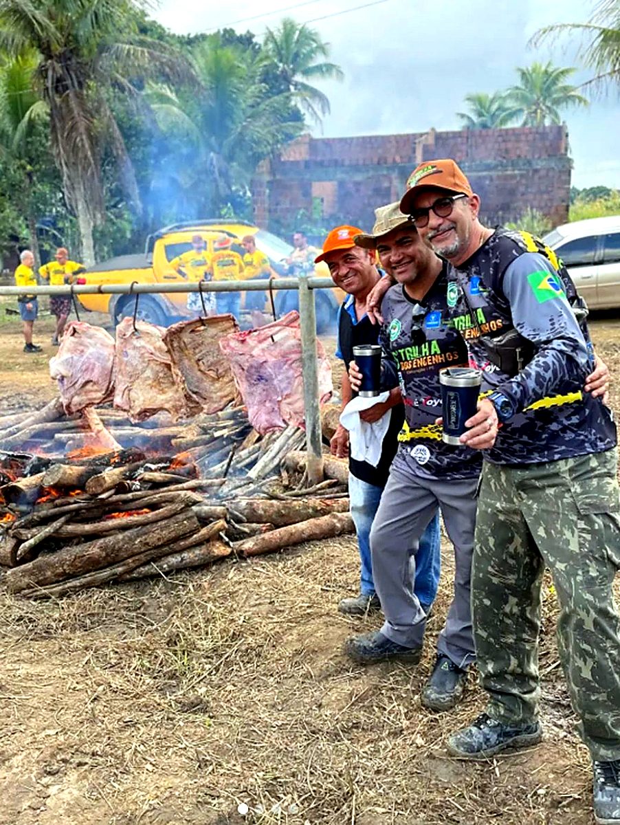 Três pilotos posando com tulipas em frente às costelas no fogo de chão — o coração do churrasco da Trilha